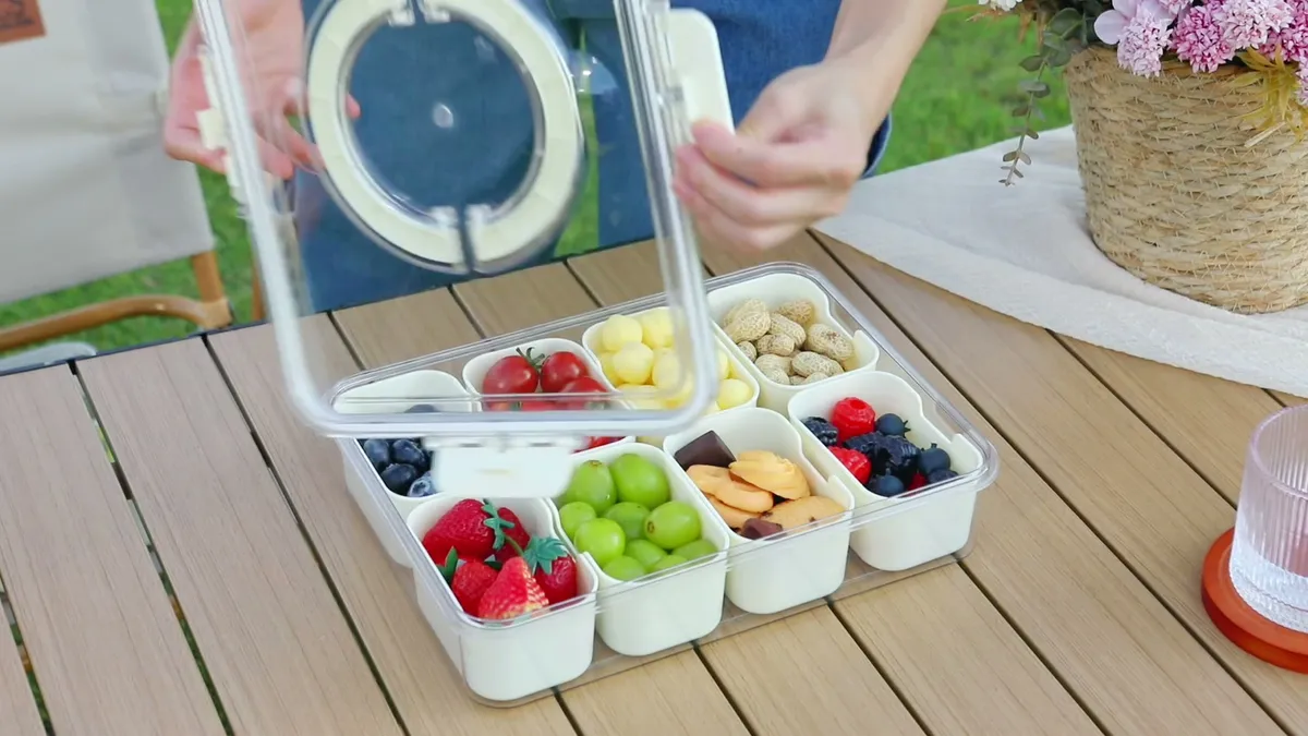 Opening the Snackle Box lid on a garden table: berries, grapes, fruit and nuts in its compartments