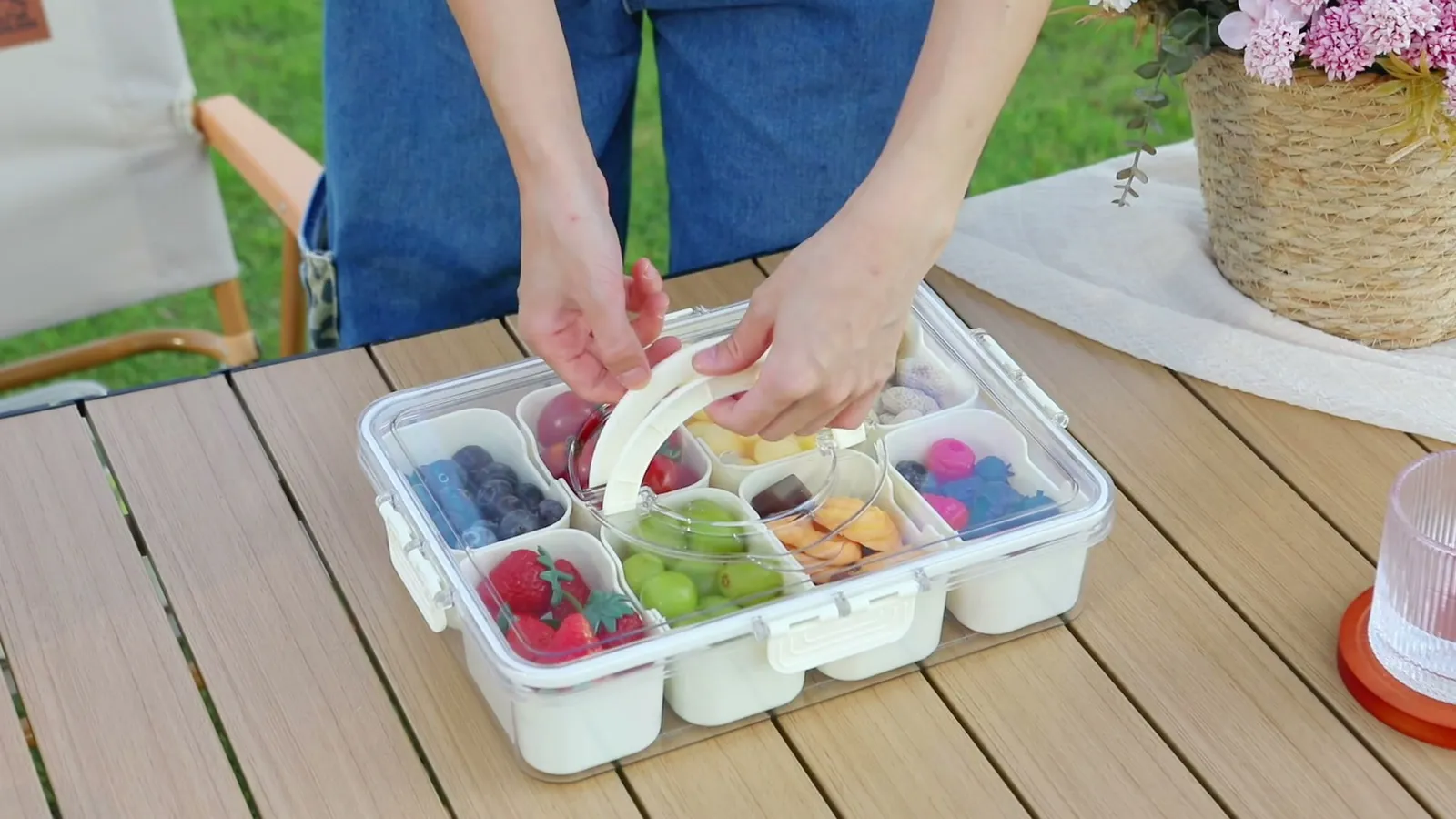 Hands carrying a Snackle Box by its handle to a garden table